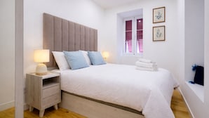 Une chambre à coucher comprenant un lit, des lampes de chevet, une table de chevet, une fenêtre avec des volets et une étagère fixée au mur.
