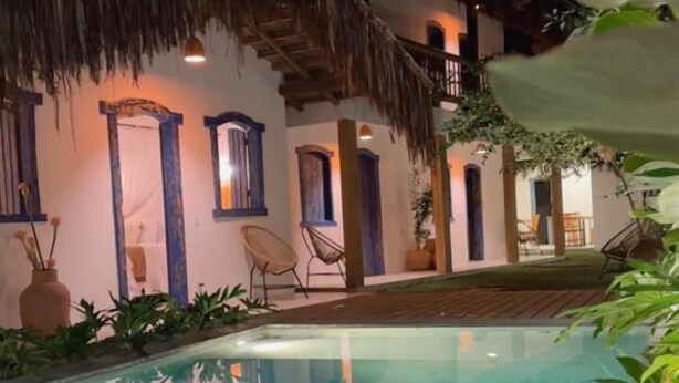 Vista nocturna de un área de piscina con una construcción de techo de paja, una piscina cristalina y abundante vegetación.
