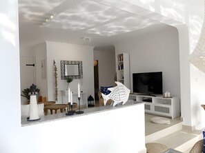A modern living room with a TV, white furniture, a fireplace, and a decorative mirror.