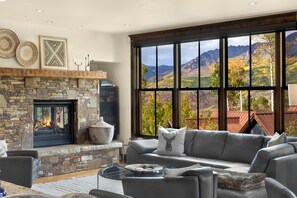 A living room with a stone fireplace, a gray sofa, and a large window with a mountain view.