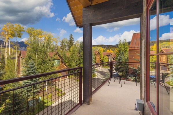 A balcony with a view of a mountainous landscape, wooden buildings, and a clear sky.