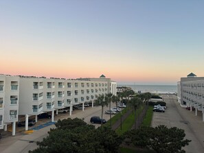 A multi-story hotel with a parking area and a view of the ocean at sunset. - Beautiful Galveston oceanfront, ocean views and heated pools.  (Galveston)