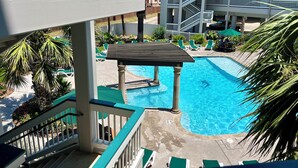 Ein Hotelpoolbereich mit einem klaren, blauen Pool, grünen Liegestühlen und einem mehrstöckigen Gebäude im Hintergrund.