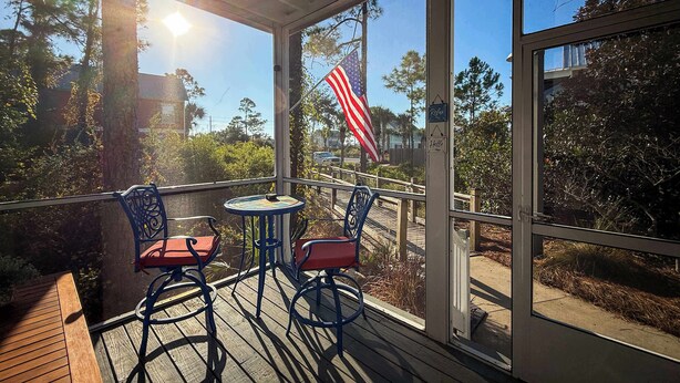 A covered outdoor seating area with a table and chairs, a wooden deck, and a view of the surrounding landscape including trees and a flag. - NEW The Funky Oyster A4 w/Pool access Port  St Joe (Port St. Joe)