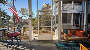 A covered outdoor area with a wooden deck, a table with chairs, a bench with cushions, and a large window overlooking a residential area. - NEW The Funky Oyster A4 w/Pool access Port  St Joe (Port St. Joe)