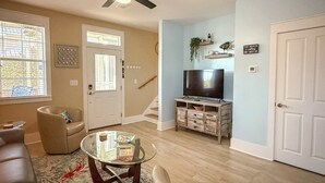 A living room with a ceiling fan, a television on a wooden stand, a glass coffee table, a beige sofa, and a patterned rug. - NEW The Funky Oyster A4 w/Pool access Port  St Joe (Port St. Joe)
