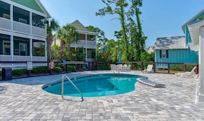 A pool area with a clear blue pool, lounge chairs, and a two-story building with balconies.