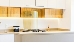 A modern kitchen with white cabinetry, a gas stove, and a black trash bin. - Praia Brava | Central Itajaí & Balneário Camboriú | 2 Bedrooms, Air Conditioning, Parking Space (Itajaí)
