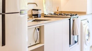 A modern kitchen with a built-in microwave, stove, sink, and a washing machine. - Praia Brava | Central Itajaí & Balneário Camboriú | 2 Bedrooms, Air Conditioning, Parking Space (Itajaí)