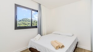 A bedroom with a large window, a bed with white linens, and a view of greenery outside. - Praia Brava | Central Itajaí & Balneário Camboriú | 2 Bedrooms, Air Conditioning, Parking Space (Itajaí)