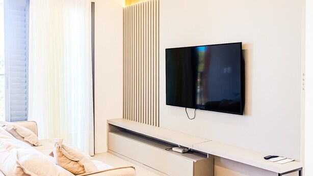 A modern living room with a flat-screen TV mounted on the wall, a sofa, and a minimalist console table. - Praia Brava | Central Itajaí & Balneário Camboriú | 2 Bedrooms, Air Conditioning, Parking Space (Itajaí)