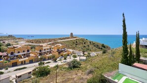 Uma vila costeira com edifícios, uma estrada e uma torre numa colina.