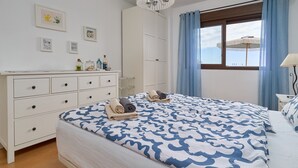 Quarto com cama, penteadeira, mesa de cabeceira e janela com cortinas.