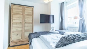 Un dormitorio con cama, armario, televisor de pantalla plana y ventana con cortinas.