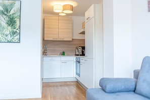 A compact kitchen with white cabinets, a dishwasher, and a stove. There is a blue sofa in the adjacent living area.
