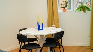 Une table de salle à manger ronde, accompagnée de quatre chaises, une fenêtre avec des rideaux et des plantes en pot.