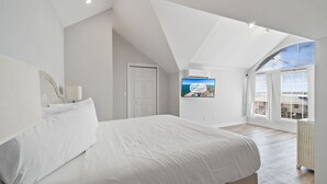 A bedroom with a large bed, a television mounted on the wall, and a view of the outside through a window.