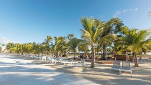 A beach with white lounge chairs and palm trees under a clear sky.