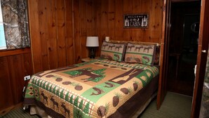 L’intérieur d’un chalet en bois, avec un lit, une pancarte de bienvenue et une lampe.
