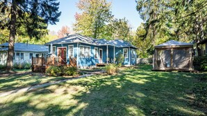 A blue house with a porch, a fenced yard, and a covered outdoor seating area.