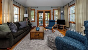 A living room with a dark-colored sofa, a blue armchair, a wooden coffee table, and a television on a stand.