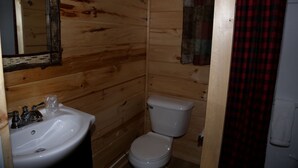 Ett badrum i en stuga, inrett med träpanel, och utrustat med handfat, toalett och spegel.