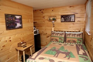 Una habitación tipo cabaña con cama, una mesita, un microondas y un cartel de bienvenida.