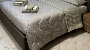 Een slaapkamer met een bed, gordijnen, een schilderij en een nachtkastje.
