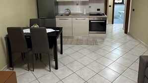 Een moderne keuken met witte kasten, een eethoek met een tafel en stoelen, en een zichtbare klok aan de muur.