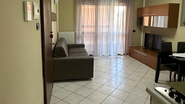 Een woonkamer met een bank, een televisie en een keuken met een fornuis.