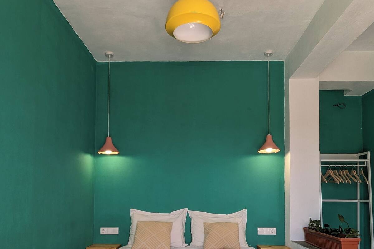 Ein Schlafzimmer mit türkis gestrichenen Wänden, einem Bett mit blauer Steppdecke, zwei Nachttischen mit Lampen und einem hölzernen Kopfteil.