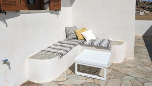 Ein weißes Gebäude mit einer Steinterrasse, einer Holztür und einem weißen Tisch mit Kissen.