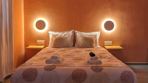 Ein ordentlich bezogenes Bett mit einem blumigen Überwurf, zwei Nachttischlampen und einer runden Deckenleuchte.