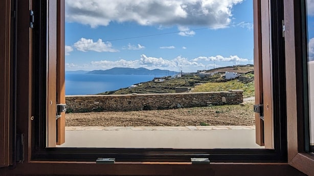 Ein Zimmer mit großem Fenster und Blick auf eine Küstenlandschaft mit Bergen und blauem Himmel.