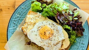 Ein Teller mit Spiegelei, geriebenem Käse und gemischtem Salat auf einem blauen Keramikteller.