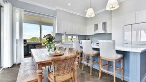 A modern kitchen with white cabinetry, a dining area with a wooden table and wicker chairs, and pendant lighting.