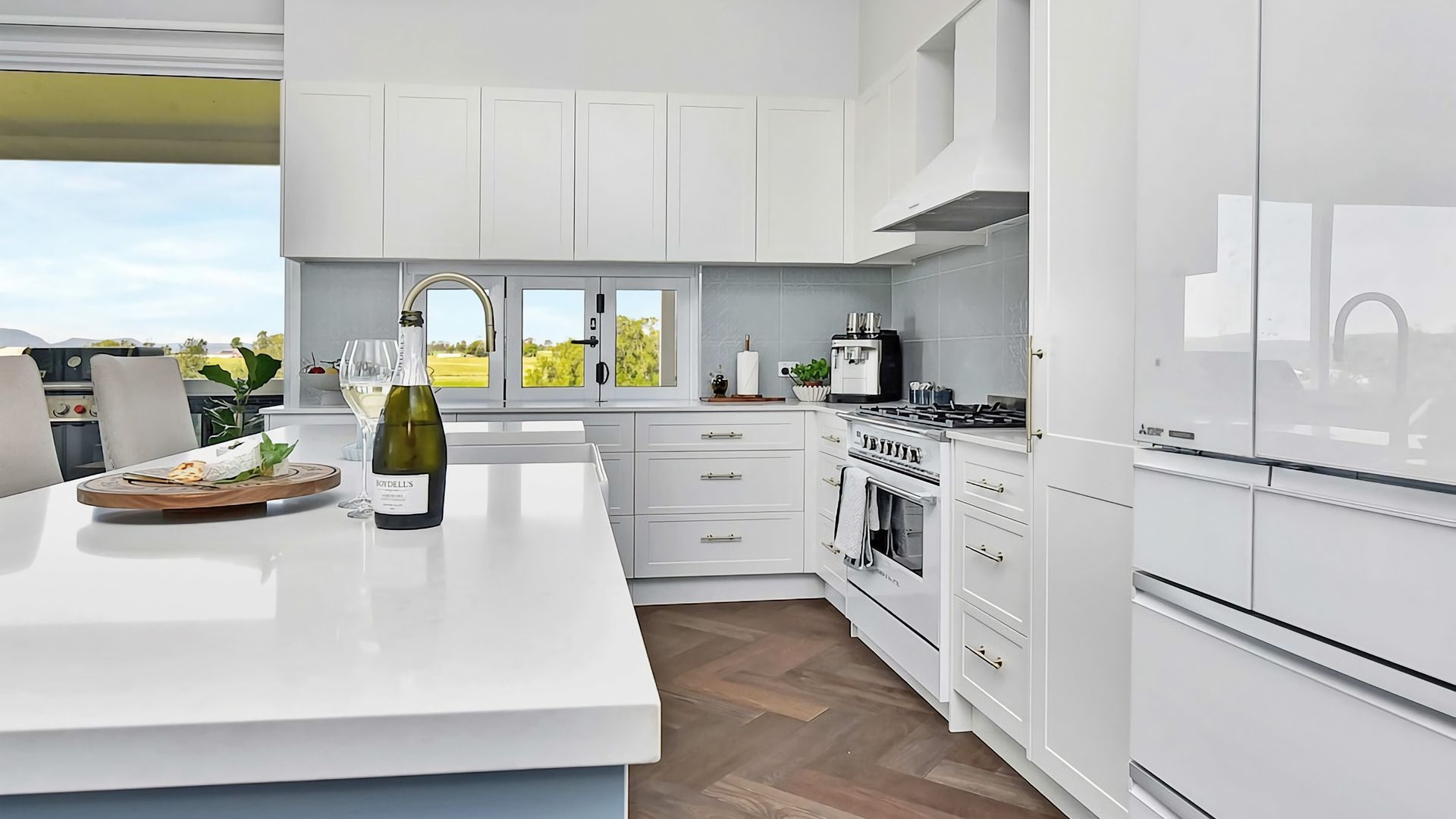 Una cocina moderna con armarios blancos, una isla central y vistas al exterior.