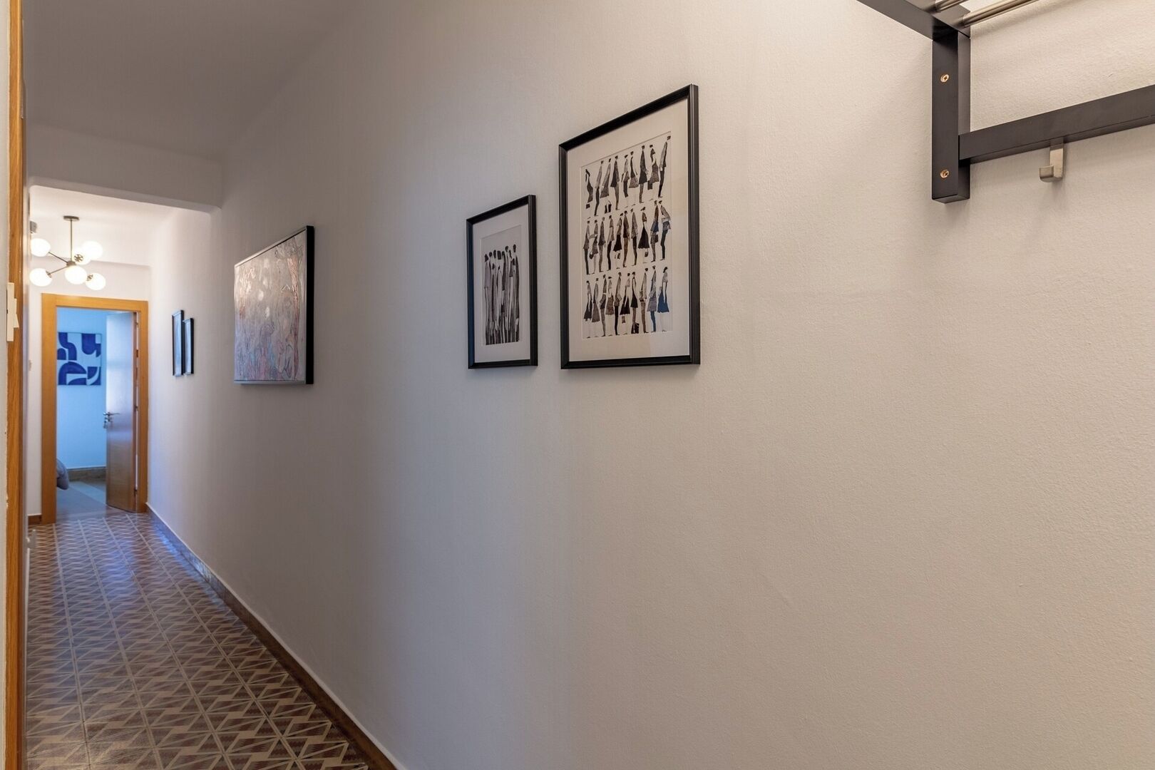 A hallway with patterned flooring, framed artwork on the walls, and a door leading to another room.