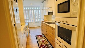 Une cuisine étroite avec des meubles blancs, un plancher en bois et un four encastré.