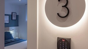 A modern hotel room with a circular wall number '3', a built-in control panel, and a glimpse of a bed and nightstand in the background.