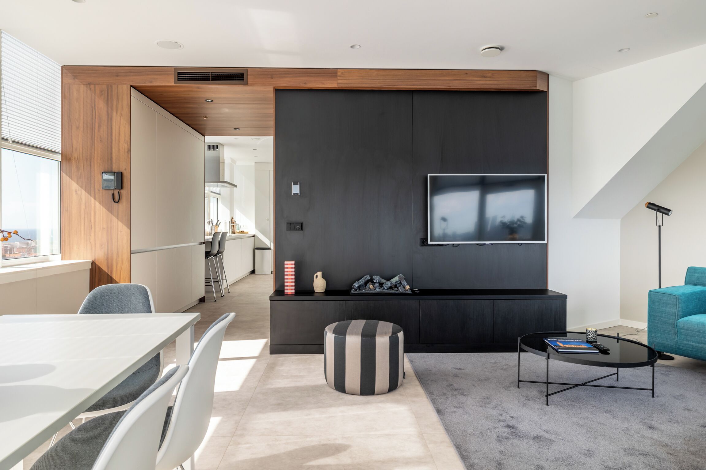 A modern living room with a dining area, a black entertainment unit, and a large TV.