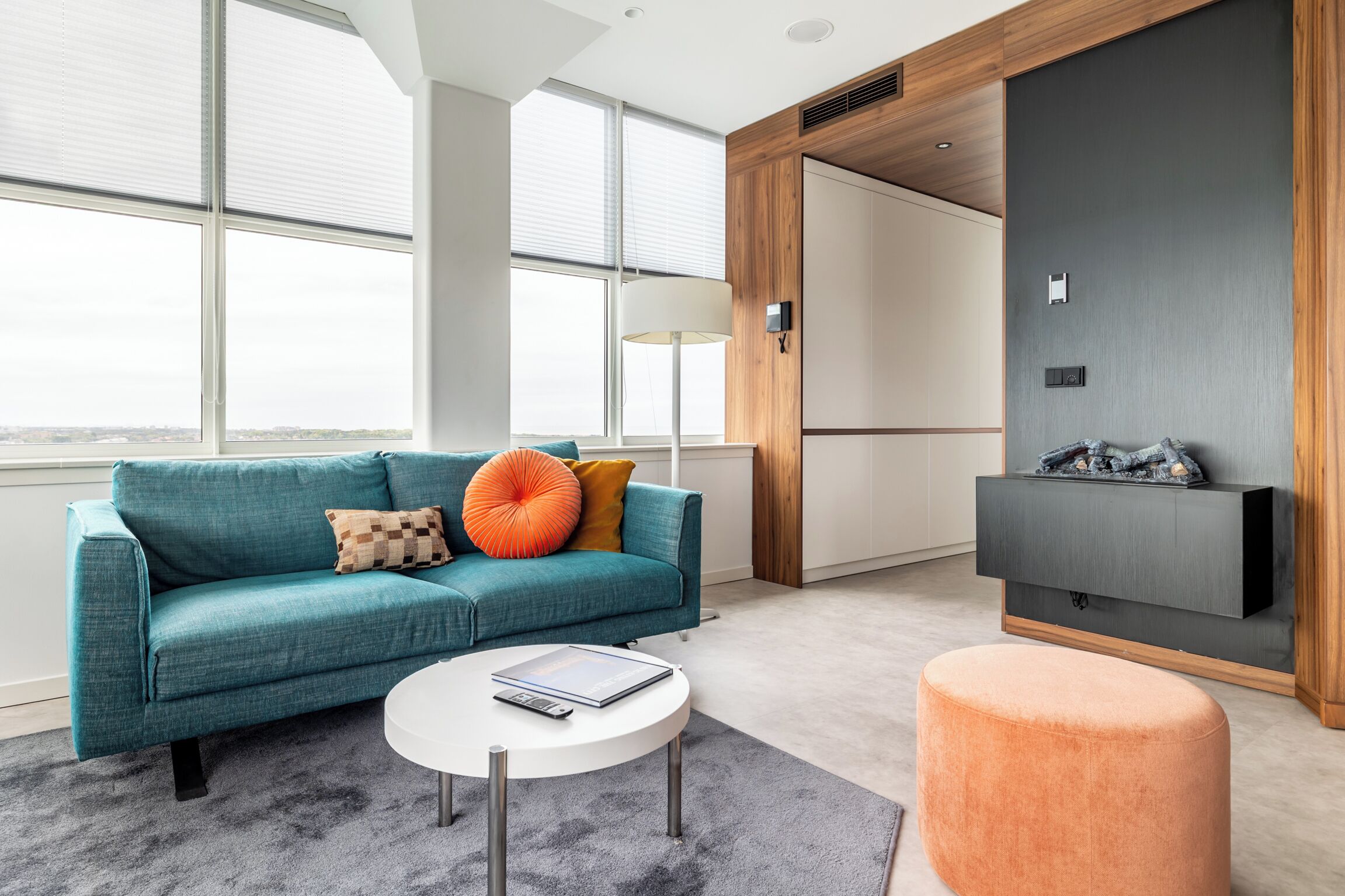 A modern living room with a teal sofa, a round coffee table, and a flat-screen TV mounted on a wooden panel wall.