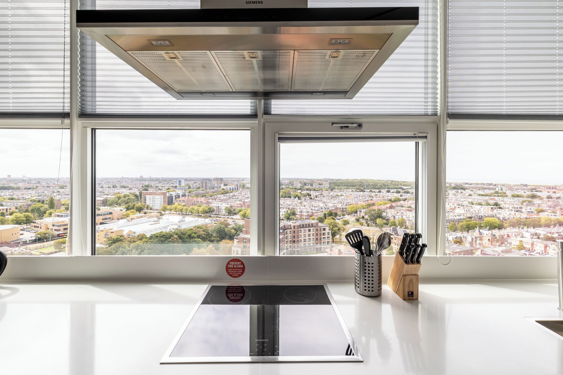 Una cucina con vista sulla città attraverso ampie finestre, una cappa aspirante in acciaio inox e un portachiodi sul bancone.