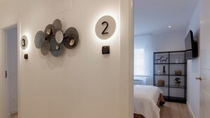 Un pasillo con un cartel con el número 3, un cartel con el número 2, y una puerta que da a un dormitorio con una cama y un televisor.