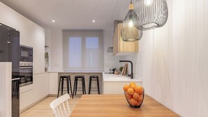 Una cocina moderna con armarios blancos, una mesa de comedor de madera y un frutero.