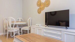 A room with a wooden table, white chairs, a TV, and a wall-mounted woven decoration. - AH Apartment Urban Lena VUT-6048-AS (Pola de Lena)