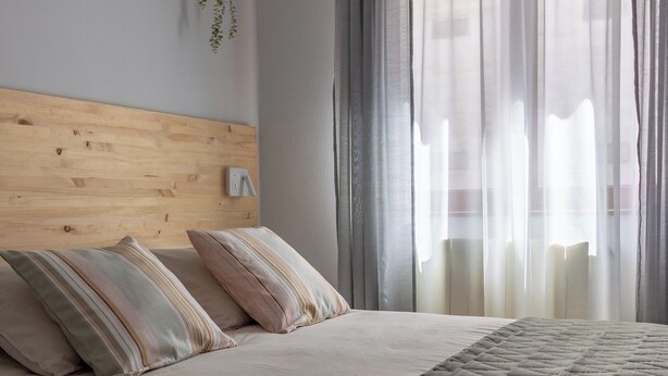 A bedroom with a wooden headboard, two striped pillows, a beige bedspread, and sheer curtains. - AH Apartment Urban Lena VUT-6048-AS (Pola de Lena)