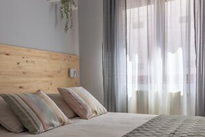 Une chambre à coucher avec une tête de lit en bois, deux coussins à rayures, une couvre-lit beige et des rideaux transparents.