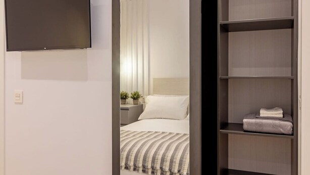 Una habitación de hotel moderna con cama, televisor montado en la pared y armario empotrado.