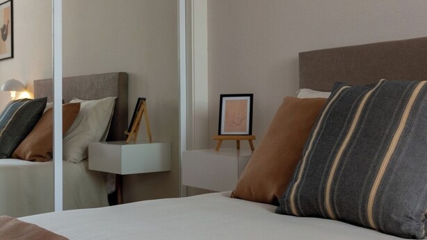 Een keurig opgemaakt slaapkamer met een bed, nachtkastjes en een spiegel.